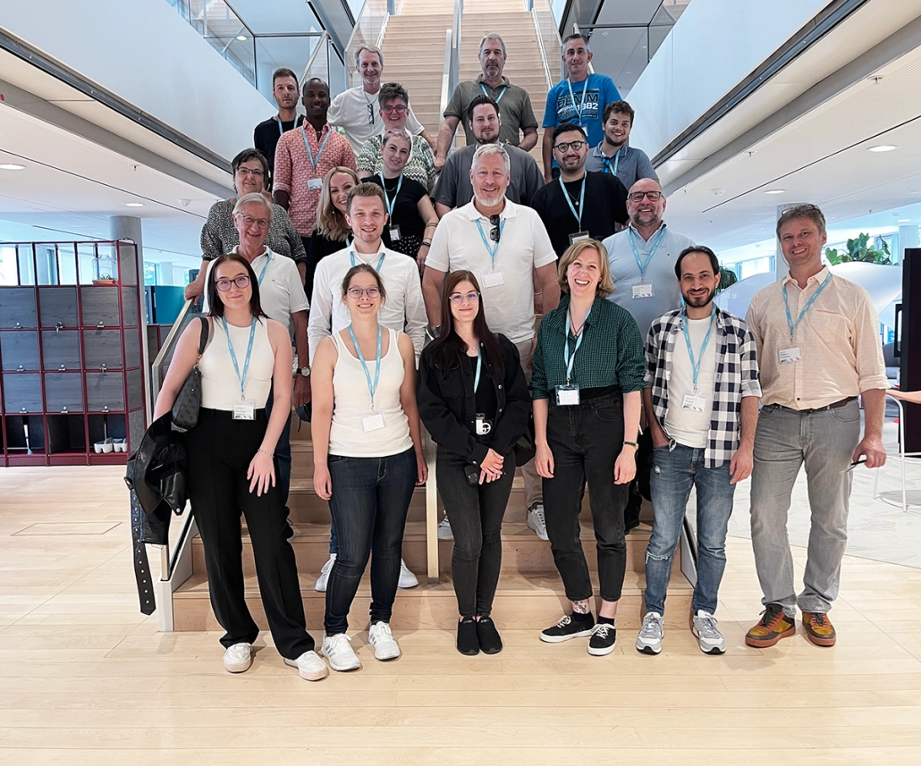 Auf dem Bild sieht man 20 Mitarbeitende von AURA. Sie stehen auf einer Treppe im LINC/München. 